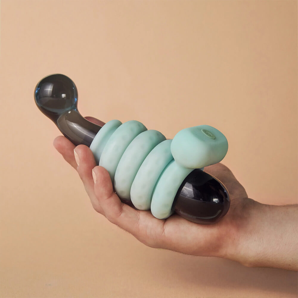 A glass or acrylic dildo is held in someone's hands. The OhNut and the Vibrating OhNut are wrapped around the dildo, showcasing how the rings all fit together for a secure, non-slip fit. The rings look squishy and soft, and they don't look like they're constricting the dildo at all. | Kinkly Shop