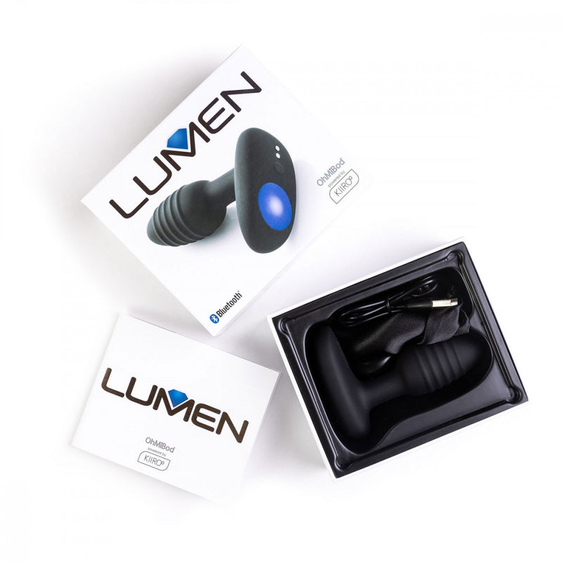 Top-down view of the OhMiBod Lumen shows the butt plug within its plastic tray packaging with the storage bag, instruction manual, and charging cable. | Kinkly Shop