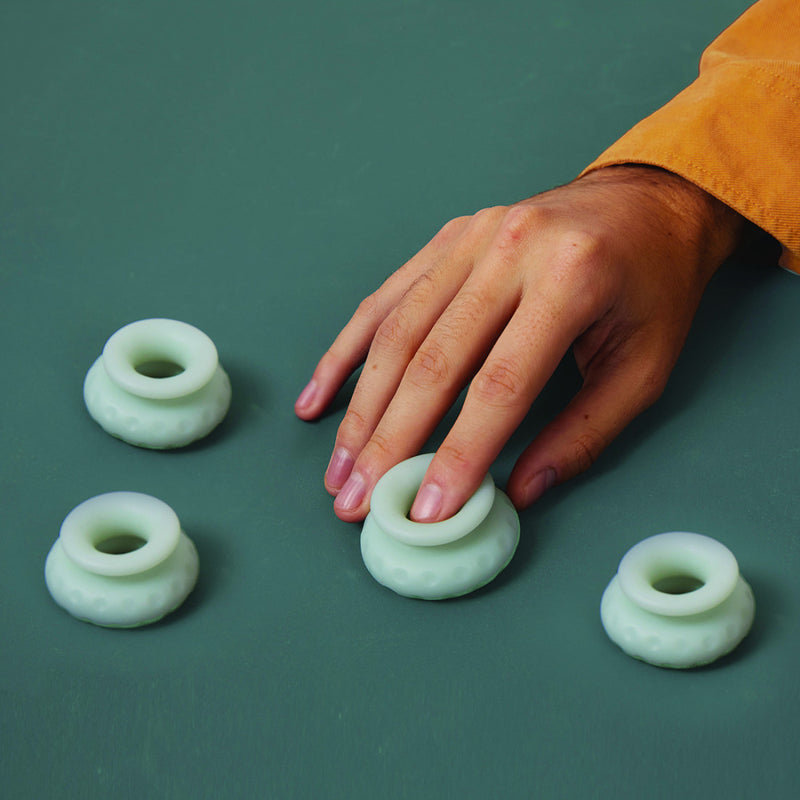 The light green OhNut Penetration Buffer Penis Limiter rings sit out on a dark green surface. A hand fiddles with one of the rings that shows that the rings are about the size of a pointer finger when entirely at-rest to fit a wide variety of penis widths. | Kinkly Shop