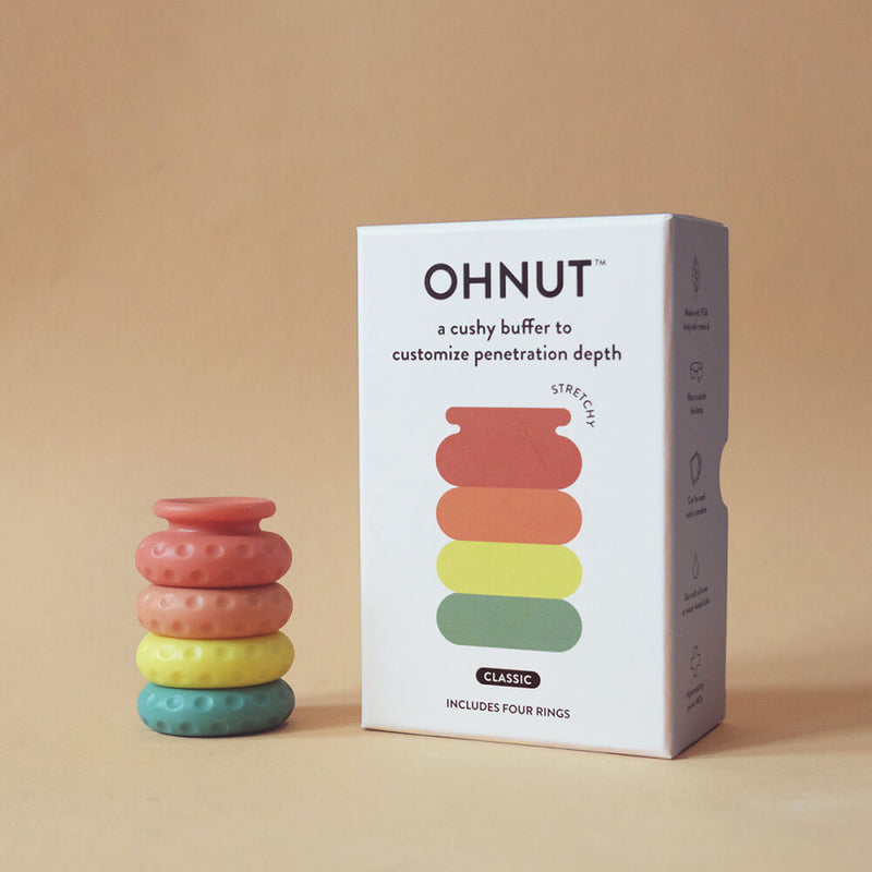 The OhNut Penetration Buffer Penis Limiter in Standard Rainbow sit out in a stack next to their packaging. | Kinkly Shop
