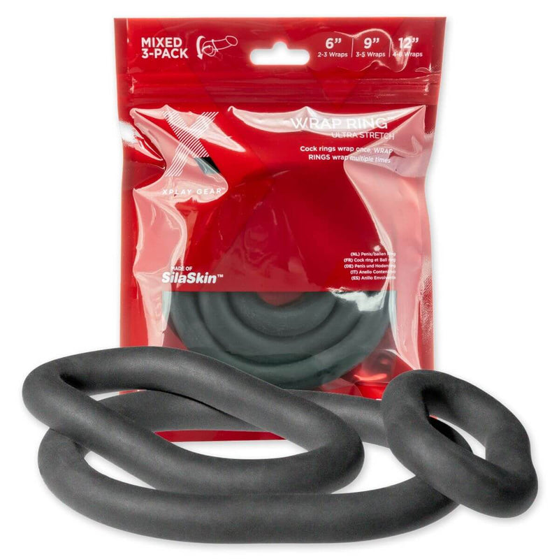 The Perfect Fit XPlay Ultra Wrap Ring Pack cock rings are all laying out in a jumbled pile in front of the packaging where another set of rings is currently contained. | Kinkly Shop