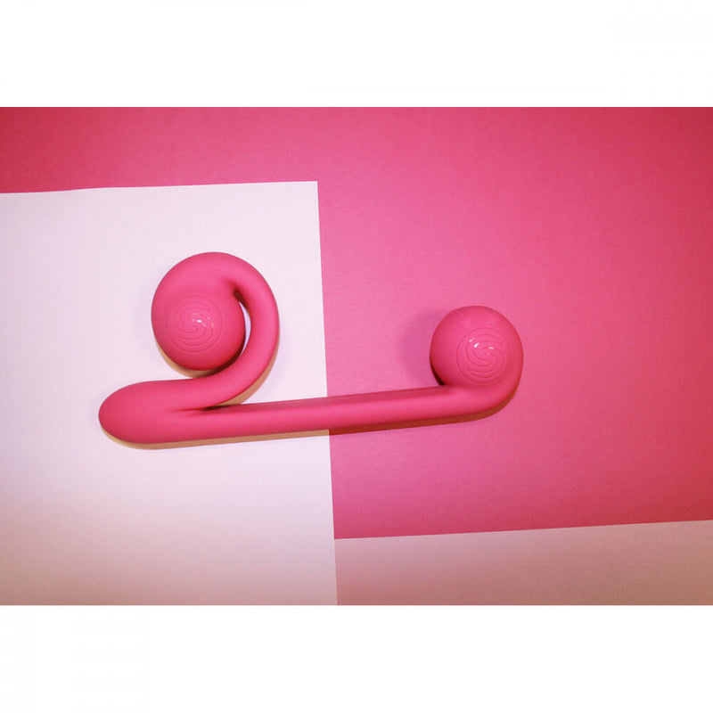 Another lifestyle image of the Snail Vibe sex toy shows this vibrator laying on top of two different shades of pink paper. | Kinkly Shop