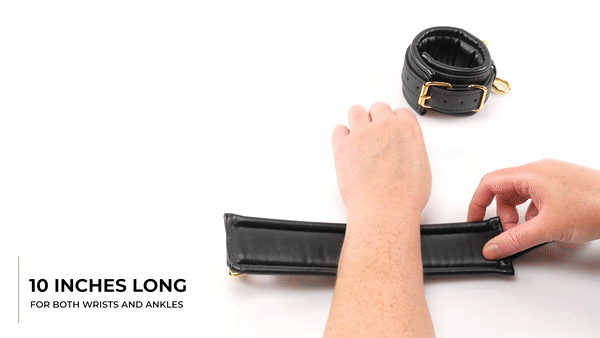 GIF of the Sportsheets Cuffs and Blindfold Set. A wrist is placed on a white table. The person uses their other, free hand to wrist up the wrist in one of the cuffs and then gives the attached golden fastener a hard tug to show stability. The text on the GIF reads "10 Inches Long for Both Wrists and Ankles." | Kinkly Shop