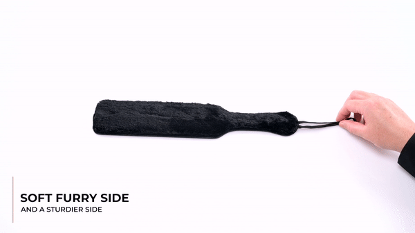 GIF of the Sportsheets Leather Paddle with Black Fur Side. GIF shows a person picking up the paddle, showing off the sheen of the leather side and the fluff of the faux fur side, and then spanking their palm with the paddle. Text reads "Soft furry side and a sturdier side". | Kinkly Shop
