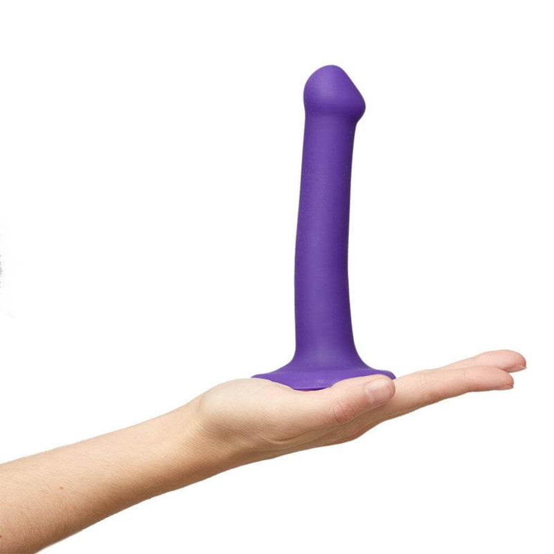 A hand is laid flat in front of the camera. The Strap-on-Me Bendable Dual-Density Dildo is resting on top of the hand to show a size comparison. | Kinkly Shop
