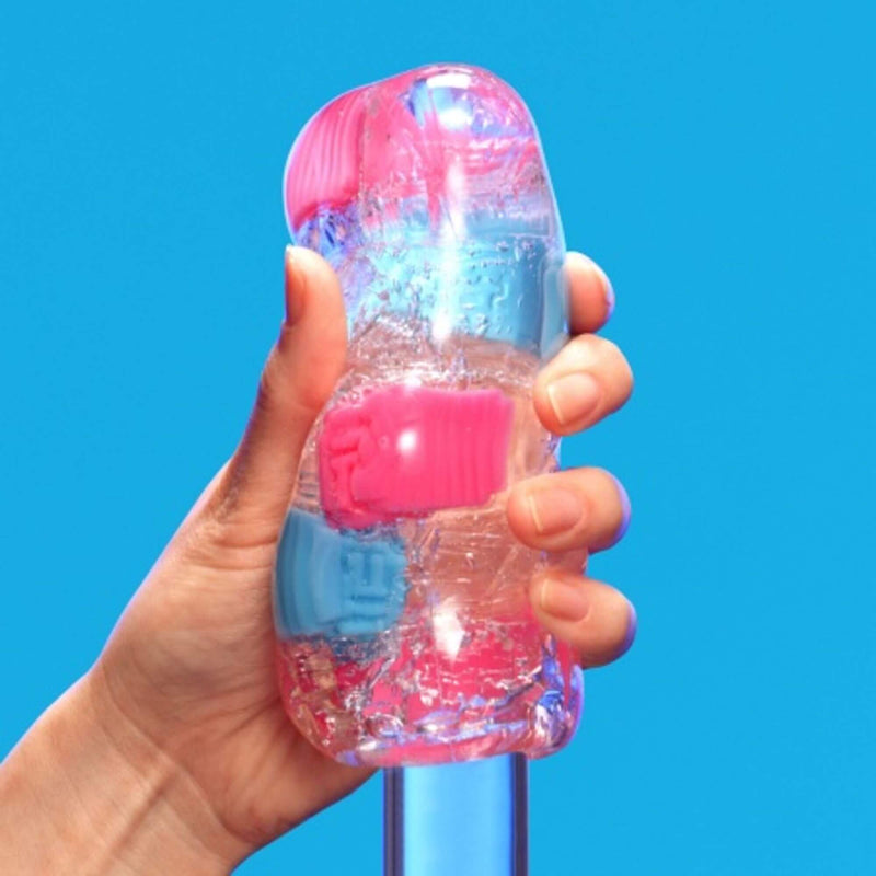 A hand holds the Tenga Bobble while the toy is being slid onto a clear, see-through glass dildo. The nodules visibly protrude away from the glass dildo to showcase the different textures. | Kinkly Shop