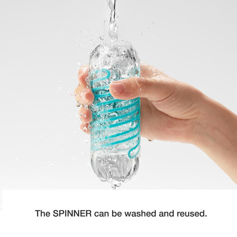 A hand holds a Tenga Spinner under the water. It shows the water pouring into the Spinner. The caption underneath the image says "The Spinner can be washed and reused". | Kinkly Shop