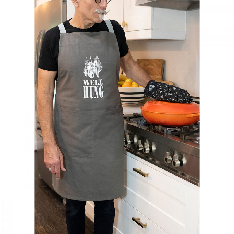 Person with awesome handlebar moustache standing in front of the oven while wearing the Twisted Wares Well-Hung Apron | Kinkly Shop
