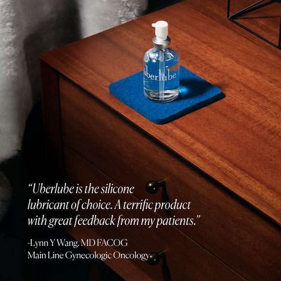 Überlube 50ml long lasting silicone lube sitting on top of a blue coaster on top of an end table. A quote reads "Uberlube is the silicone lubricant of choice. A terrific product with great feedback from my patients" attributed to Lynn W Wang MDFACOG. | Kinkly Shop