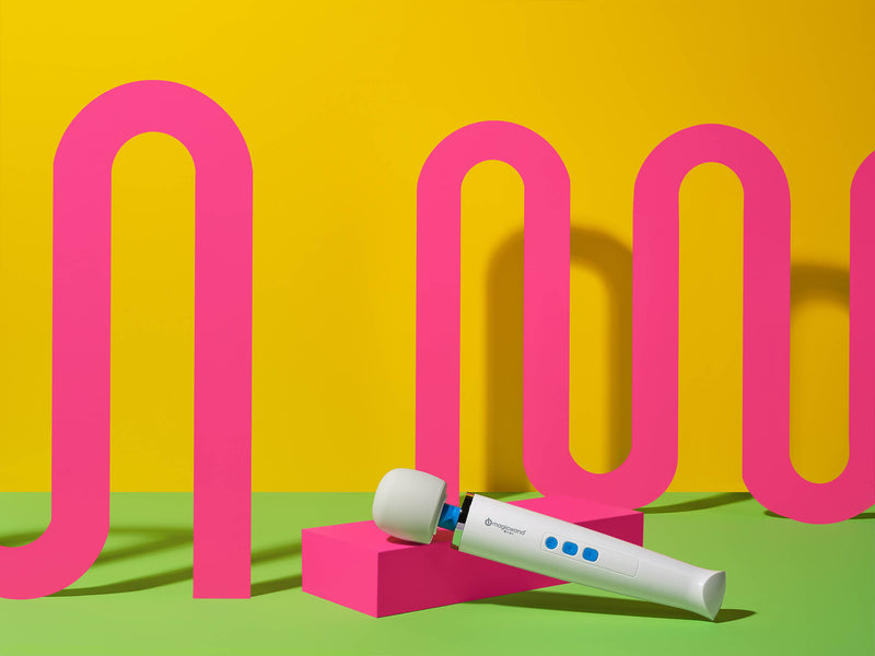 The Vibratex Magic Wand Mini Wand Massager laying down in front of cool geometric patterns. The ground is lime green while the background is canary yellow. Undulating pink waves go from the left to the right side of the frame - behind the Wand. | Kinkly Shop