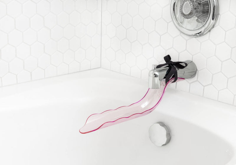 The Waterslyde Bathtub Water Diverter is shown tied onto a bathtub faucet located in an immacuately clean white bathtub. | Kinkly Shop