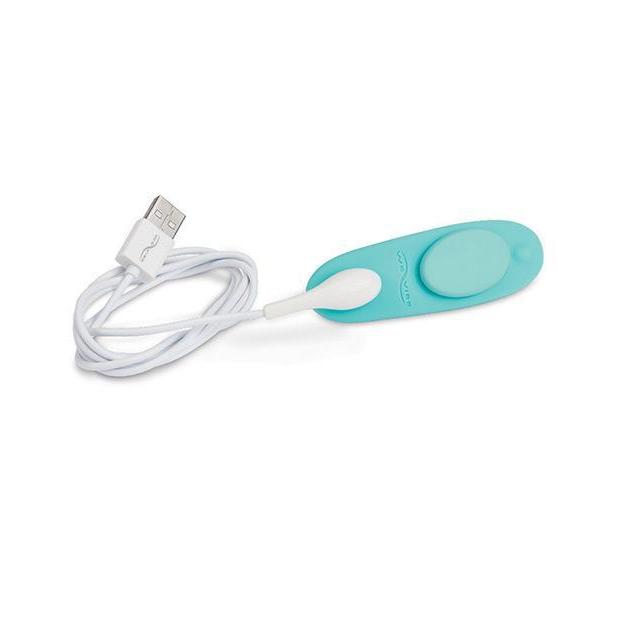 We-Vibe Moxie+ Panty Vibe in Aqua laying against a white background with the magnetic charging resting on the charging port for the vibrator. This showcases how the magnetic charging functionality works. | Kinkly Shop