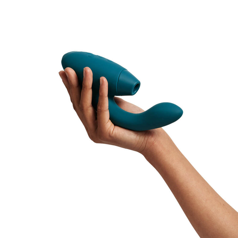 A hand holds the Womanizer Duo 2 at 3/4ths angle. This showcases the air suction hole as well as the upwards curve of the g-spot shaft. The vibrator is longer than it seems, too, with the toy extending beyond the base of the palm. | Kinkly Shop
