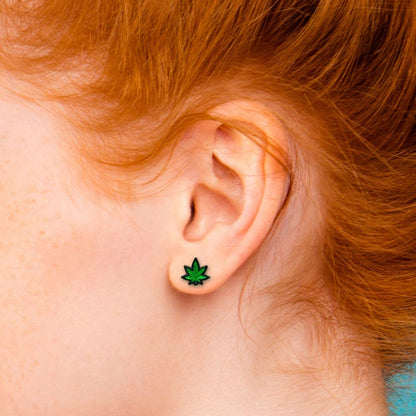 A red-headed person wears the Marijuana Leaf Earrings in their ears. It shows that the design is relatively small compared to ear size but still very visible. | Kinkly Shop